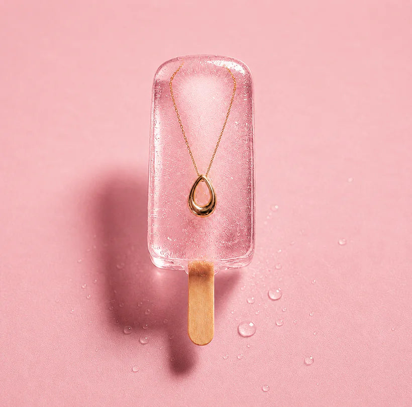 Gold teardrop necklace displayed in pink ice